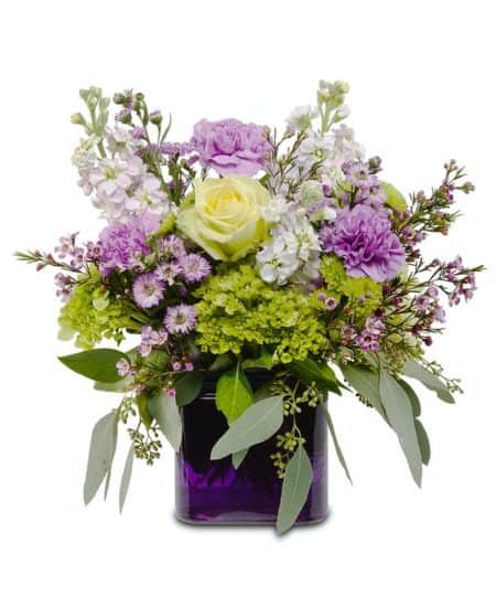 Purple glass cube vase with soft pastel tones of CARNATIONS, STOCK, HYDRANGEAS and a green ROSE.