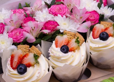 Big cupcakes with white frosting and pink flowers in background